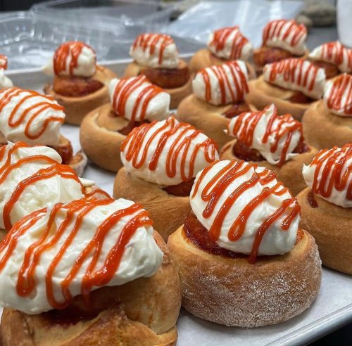 A tray of sweet rolls topped with cream and drizzled with red sauce, arranged neatly.