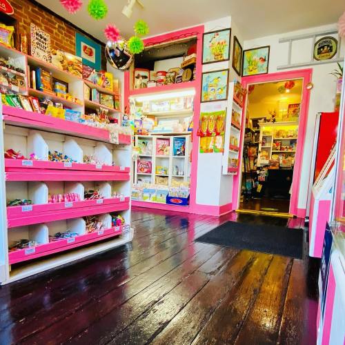 A colorful shop interior with pink shelves filled with toys and candy, featuring wooden floors and bright decorations.