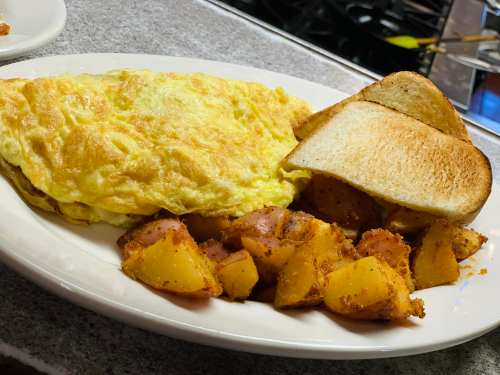 A plate of fluffy omelette, golden-brown toast, and seasoned roasted potatoes.