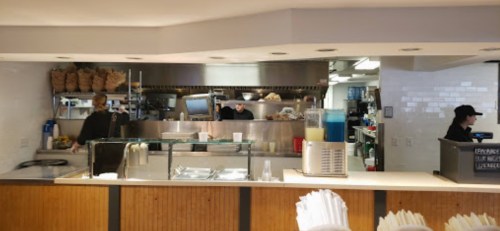 A busy restaurant kitchen with staff preparing food behind a counter, featuring various kitchen equipment and supplies.