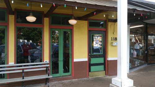 A colorful storefront with green doors and windows, featuring festive lights and a bench outside.