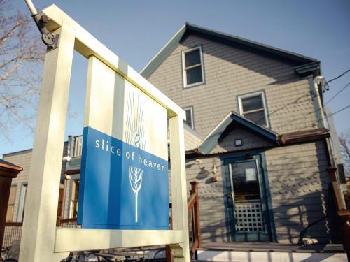 A sign reading "slice of heaven" in front of a charming blue-gray house with a porch and clear sky.