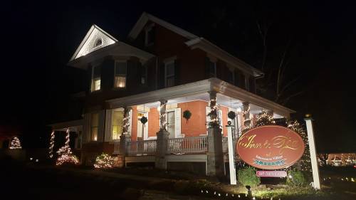 A beautifully lit historic house at night, featuring festive decorations and a welcoming sign for an inn.