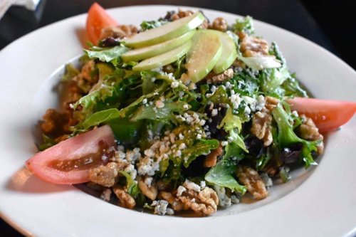 A fresh salad with mixed greens, sliced apples, walnuts, tomatoes, and crumbled cheese on a white plate.