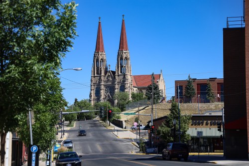 A street view featuring a church with twin spires, surrounded by trees and buildings under a clear blue sky.