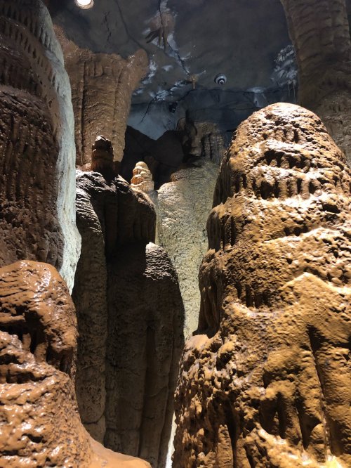 A narrow cave passage with tall, textured rock formations resembling stalagmites and stalactites.