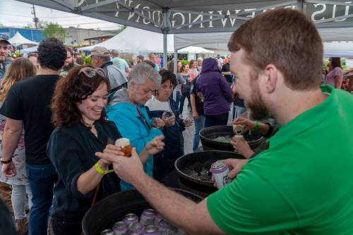 A lively outdoor event with people enjoying drinks, chatting, and socializing under tents.