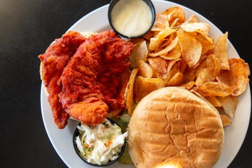 A plate featuring crispy fried chicken, homemade potato chips, coleslaw, and a soft sandwich bun.