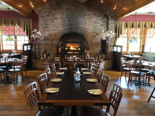 Cozy restaurant interior with wooden tables, chairs, and a large stone fireplace as a focal point.