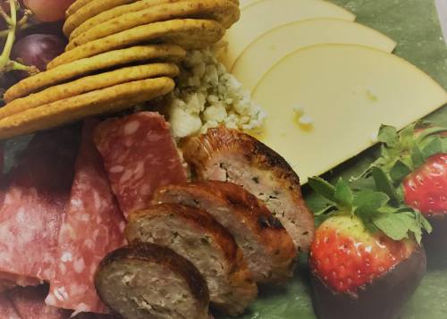 A platter featuring sliced meats, cheese, crackers, and fresh strawberries arranged on a green background.