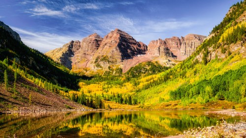 Scenic mountain landscape with vibrant autumn foliage reflected in a calm lake under a clear blue sky.