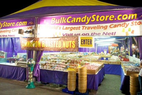 A colorful candy store tent with various candy displays and a sign promoting roasted nuts and online shopping.