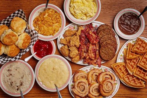 A spread of breakfast foods including biscuits, gravy, eggs, bacon, sausage, waffles, and cinnamon rolls on a wooden table.