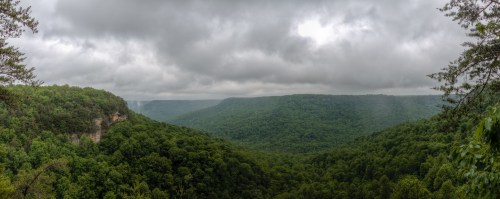 A panoramic view of lush green mountains under a cloudy sky, showcasing a serene, natural landscape.
