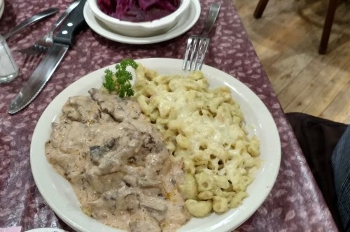 A plate of creamy beef stroganoff with noodles and a side of red cabbage on a patterned tablecloth.