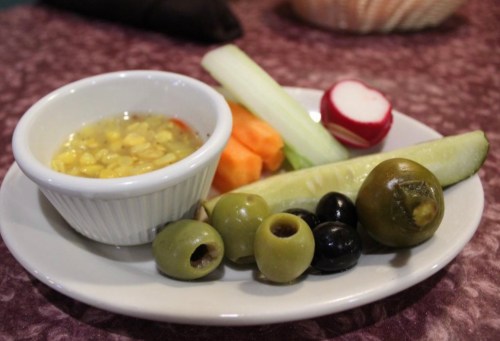 A plate with assorted vegetables, olives, and a small bowl of corn salad.