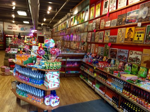 A colorful candy store with shelves of sweets, drinks, and vintage signs adorning the walls.