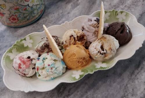 A decorative dish holds eight scoops of colorful ice cream, with two wafer sticks on top.