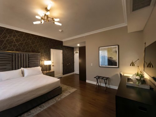 A modern hotel room featuring a king-sized bed, stylish decor, and a flat-screen TV against a dark accent wall.
