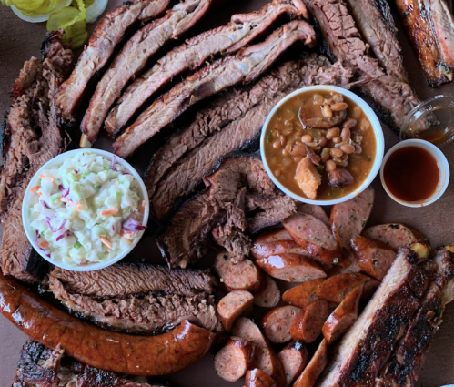 A platter of assorted barbecue meats, including brisket, sausage, and ribs, accompanied by coleslaw and baked beans.
