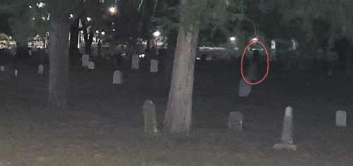 A dimly lit cemetery at night, with gravestones visible and a shadowy figure in the background.