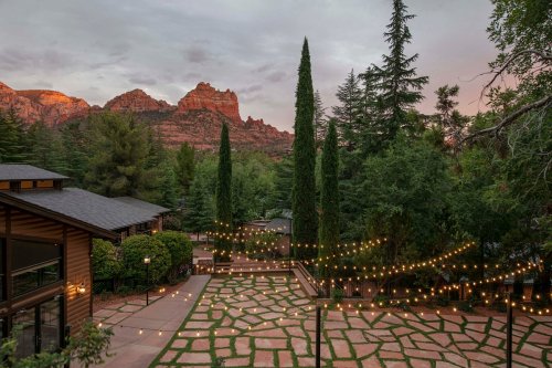 Scenic view of a landscaped area with string lights, surrounded by trees and mountains at sunset.