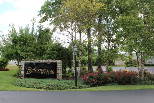 Sign for Belanere Suites surrounded by greenery and flowers, with a clear blue sky in the background.