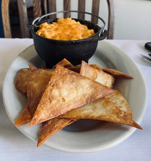 A plate of crispy triangular chips served with a small cast-iron dish of melted cheese dip.