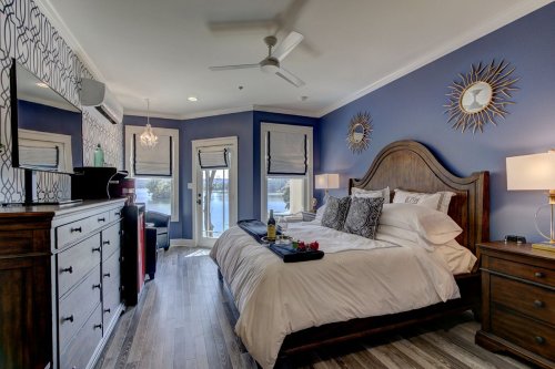 Cozy bedroom with a large bed, wooden furniture, and a view of the water through sliding glass doors.
