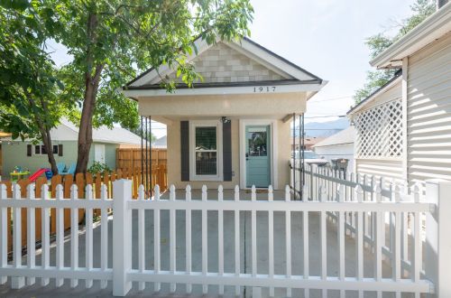 A small, charming house with a white picket fence, featuring a light blue door and surrounded by trees.
