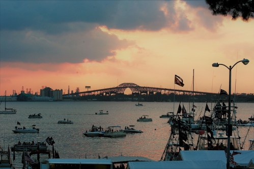 Sunset over a harbor with boats and a bridge in the background, creating a serene waterfront scene.