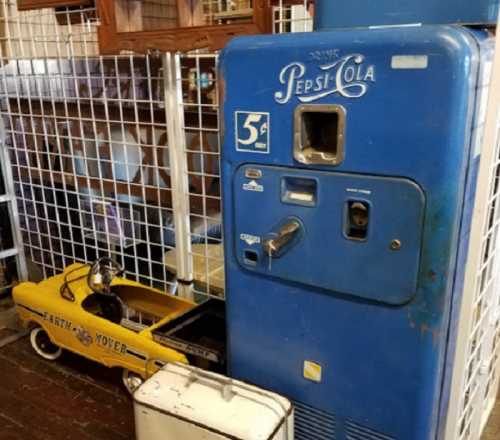 A vintage blue Pepsi-Cola vending machine next to a small yellow toy car.