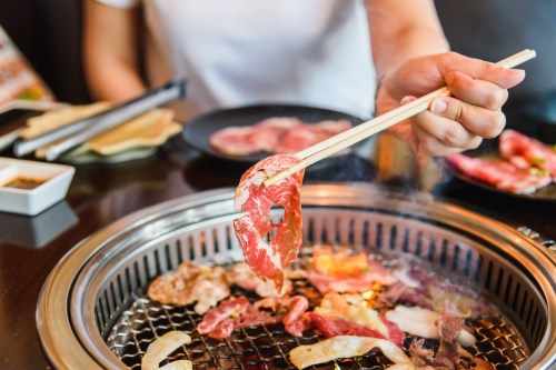 A person using chopsticks to pick up a piece of meat from a grill, surrounded by various grilled meats.