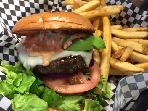 A juicy burger with cheese, lettuce, tomato, and sauce, served with crispy fries in a checkered paper basket.
