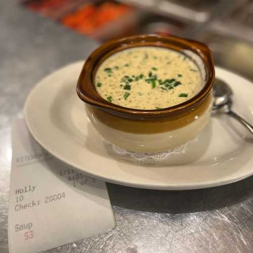 A bowl of creamy soup garnished with herbs, placed on a plate next to a receipt.