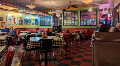A cozy restaurant interior with checkered tablecloths, colorful lights, and patrons enjoying their meals.