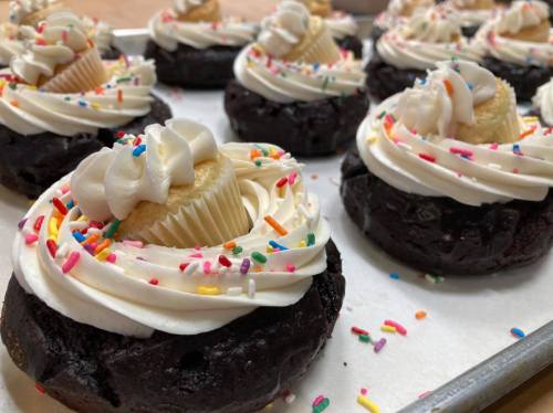 A tray of chocolate cupcakes topped with swirls of frosting, mini cupcakes, and colorful sprinkles.