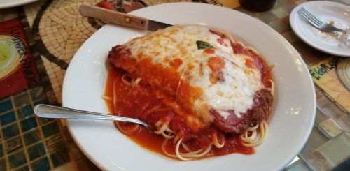 A plate of spaghetti topped with a large chicken parmesan covered in marinara sauce and melted cheese.