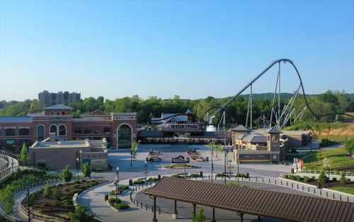 A view of an amusement park entrance with a roller coaster in the background and green trees under a clear blue sky.