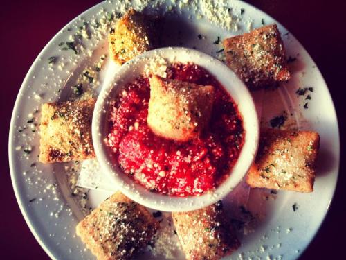 A plate of golden-brown fried snacks arranged around a bowl of marinara sauce, sprinkled with herbs and cheese.