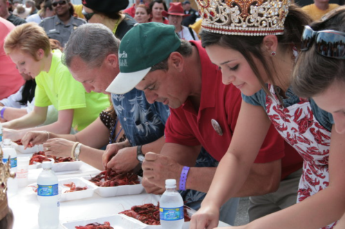 A group of people at a festival enjoying a crawfish boil, focused on peeling crawfish at a long table.