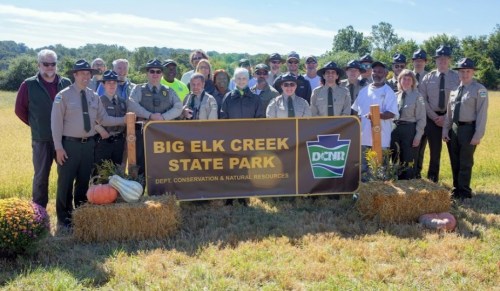 Group of park rangers and officials posing in front of a sign for Big Elk Creek State Park, surrounded by nature.