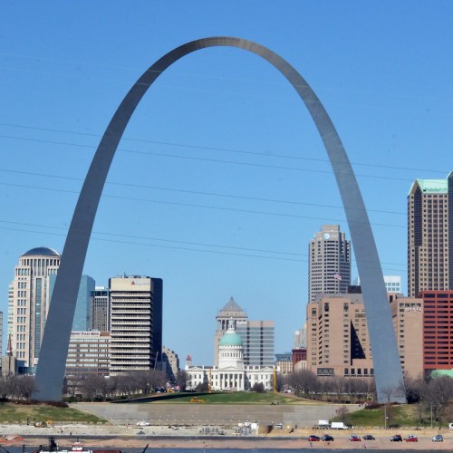 The Gateway Arch towers over the St. Louis skyline, with buildings and a green park in the foreground.