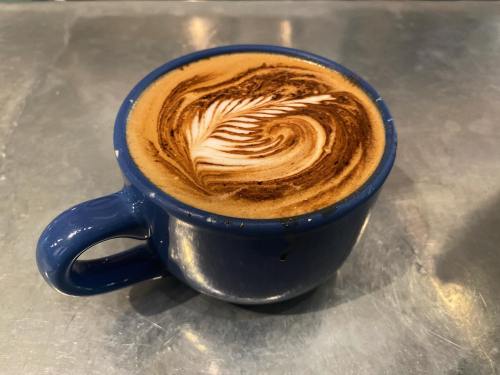 A blue coffee cup with intricate latte art featuring a swirling leaf design on a metallic surface.