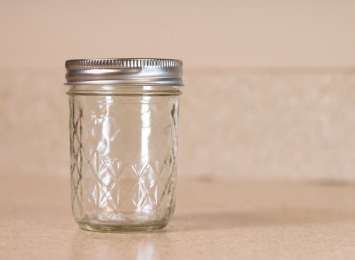 A clear glass mason jar with a silver metal lid, sitting on a light-colored countertop.