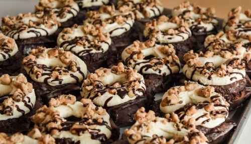 A tray of chocolate donuts topped with cream, crushed nuts, and drizzled chocolate.