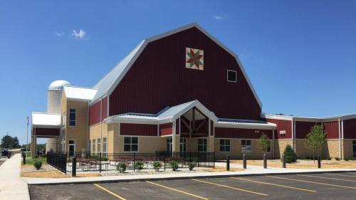 A large, red barn-style building with a colorful quilt block design on the front, surrounded by a paved parking lot.