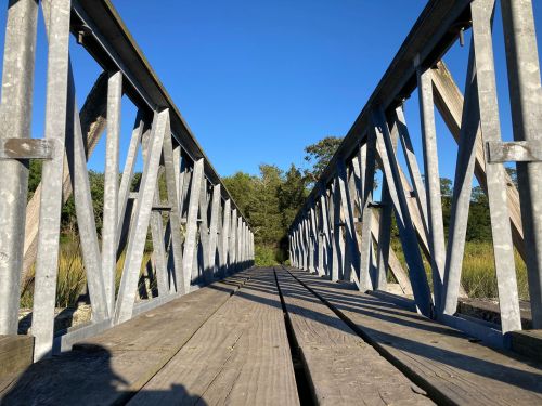 View of a metal bridge from below, with wooden planks and a clear blue sky in the background.