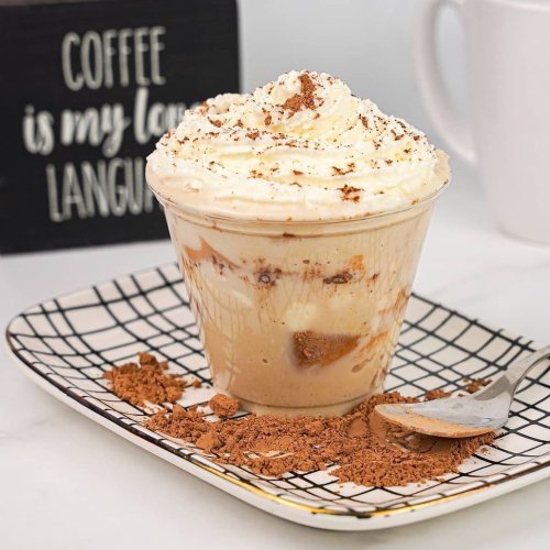 A creamy coffee dessert in a cup, topped with whipped cream and chocolate shavings, served on a patterned plate.