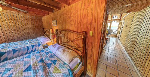 Cozy bedroom with two beds, wooden walls, and a hallway leading to a bright, open space.